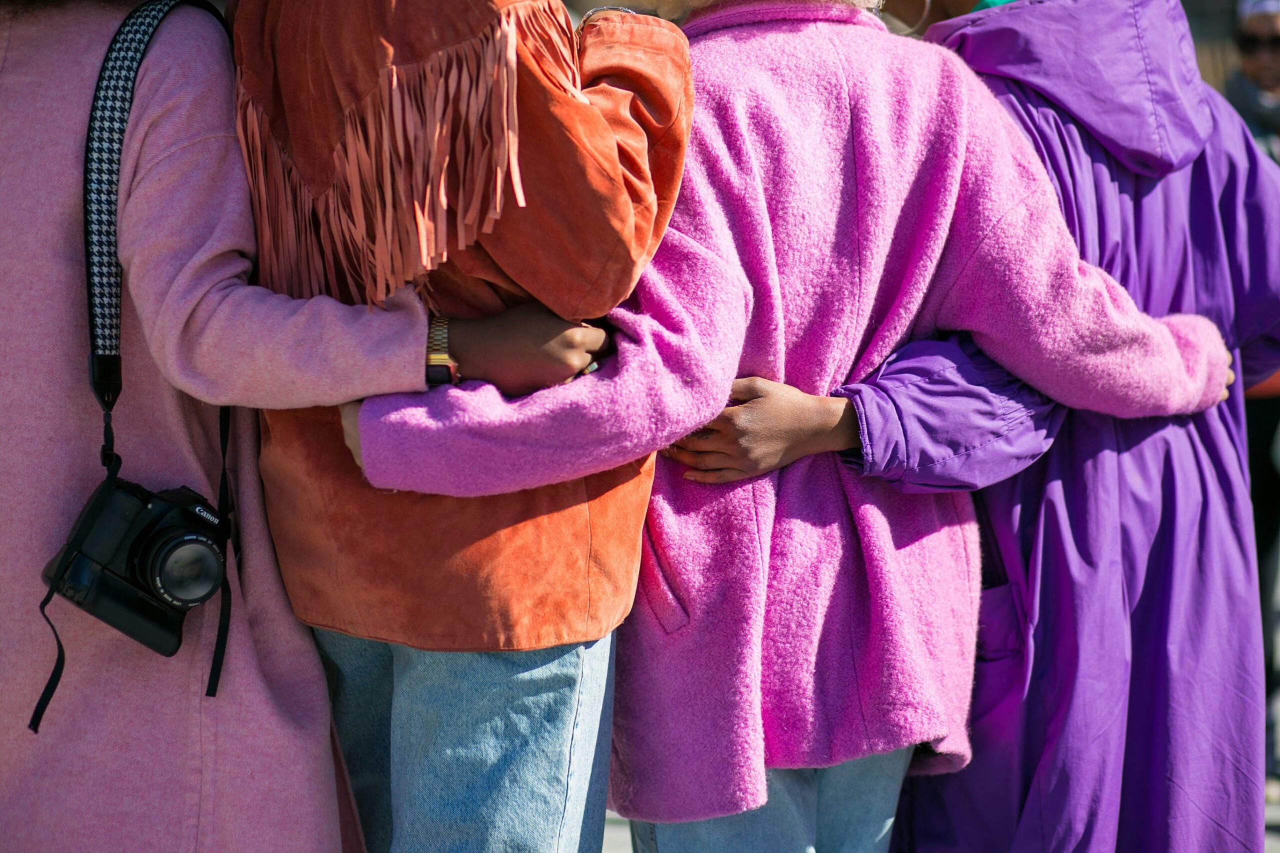 Women standing arm in arm in colorful coats